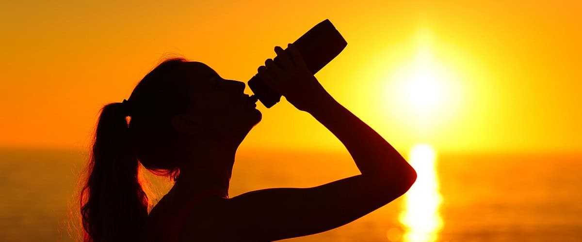 woman drinking water on beach at sunset