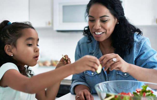 mother daughter making salad in kitchen