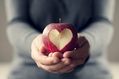 hands holding apple with a heart shape