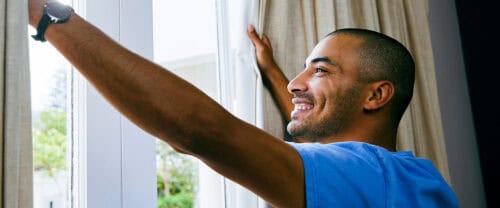 man waking up opening curtains