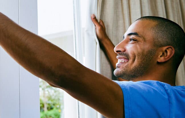 man waking up opening curtains