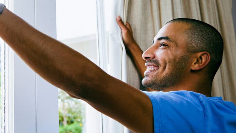 man waking up opening curtains